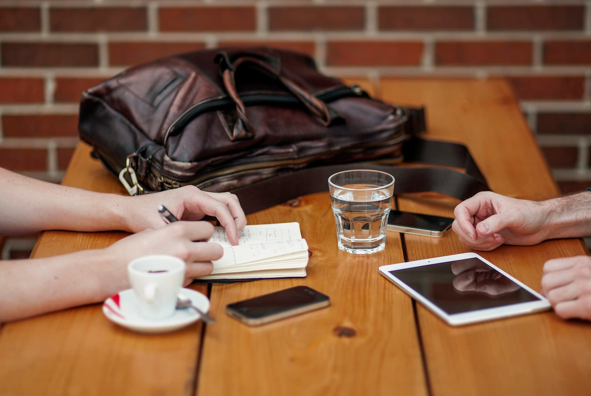 Two people taking notes during a meeting at a wooden table